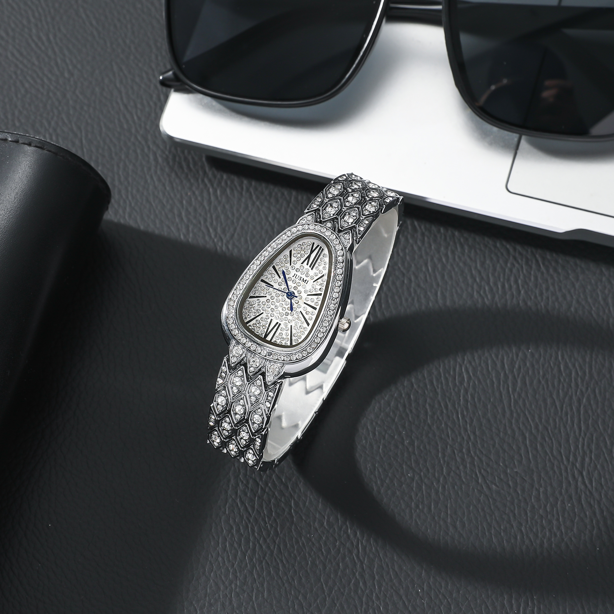 Eine elegante, mit Diamanten besetzte Uhr auf einer schwarzen Oberfläche, mit einem schwarzen Lederaccessoire und Brille.