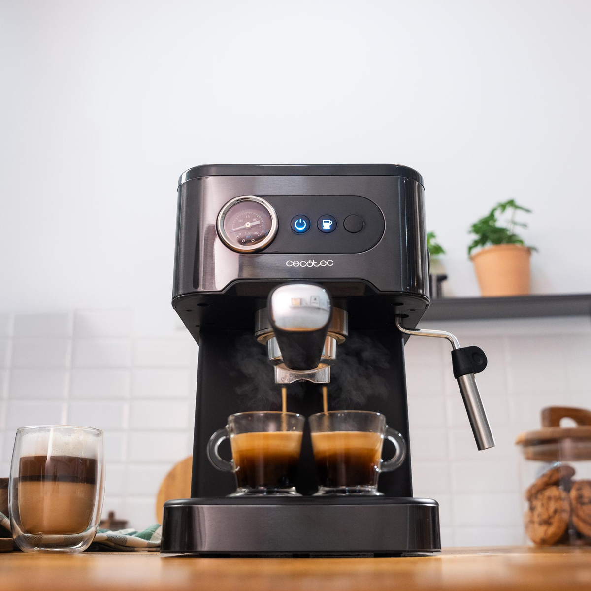 Una macchina per l'espresso prepara il caffè in due tazze di vetro. Un bicchiere di bevanda a strati è nelle vicinanze.