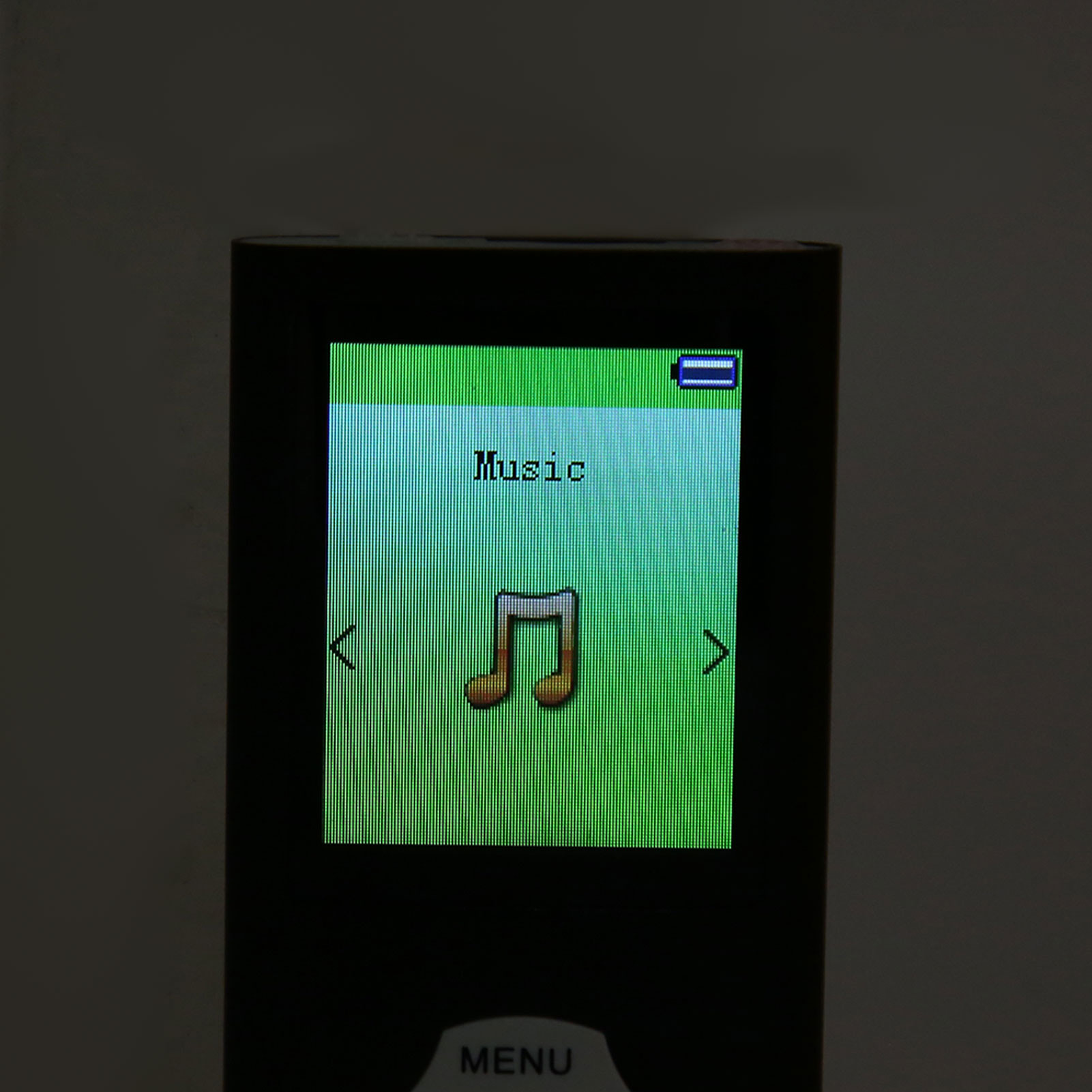 Kleiner MP3-Player. Der grüne Bildschirm zeigt 'Musik' und ein Notensymbol. Menü-Taste sichtbar.