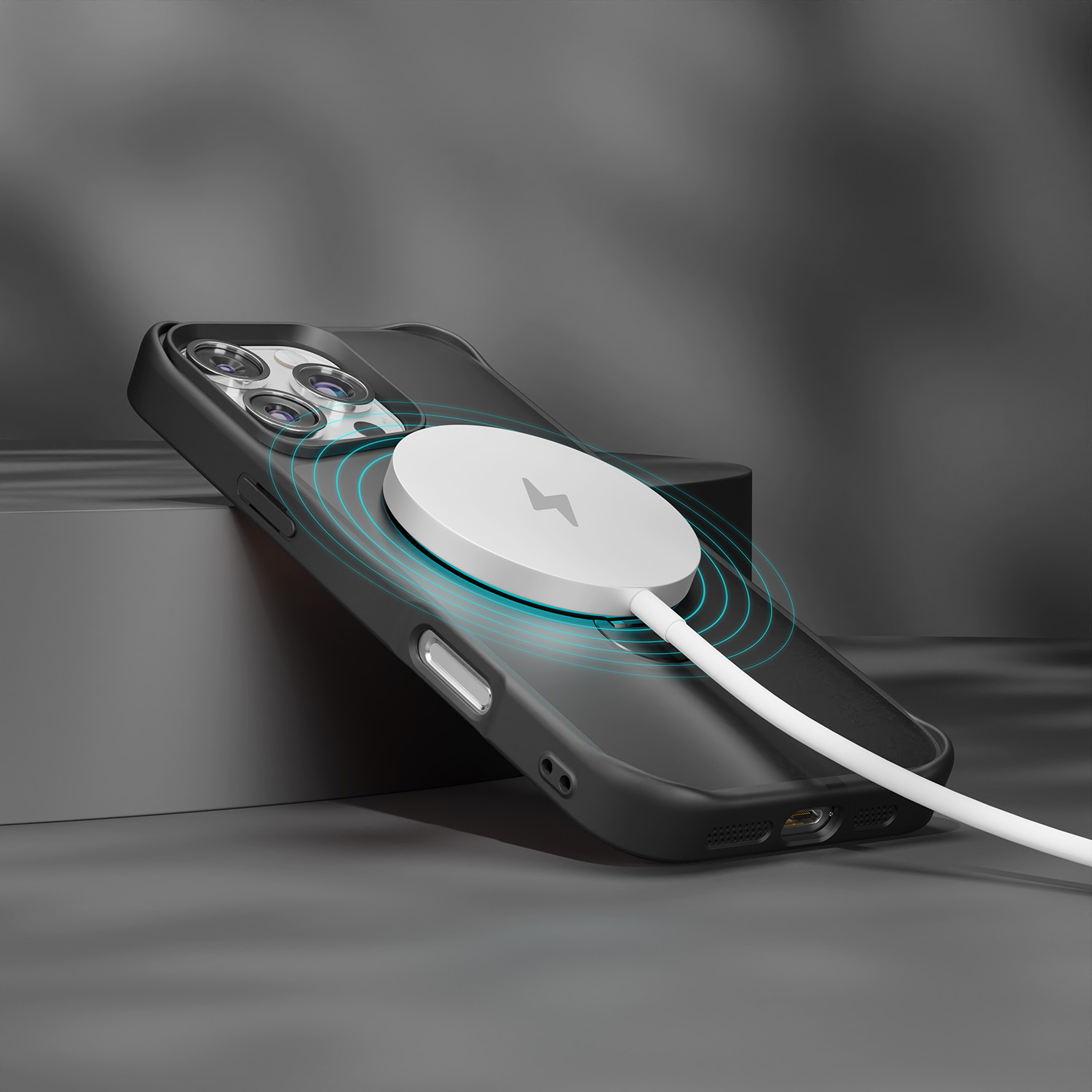 Czarne etui na telefon z białą ładowarką MagSafe i białym kablem, na ciemnoszarej powierzchni.