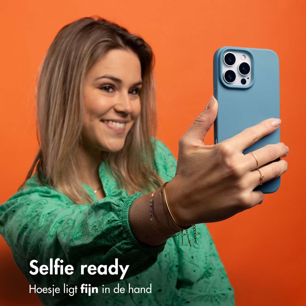 Frau macht Selfie mit blauer Handyhülle, lächelnd, auf orangefarbenem Hintergrund.