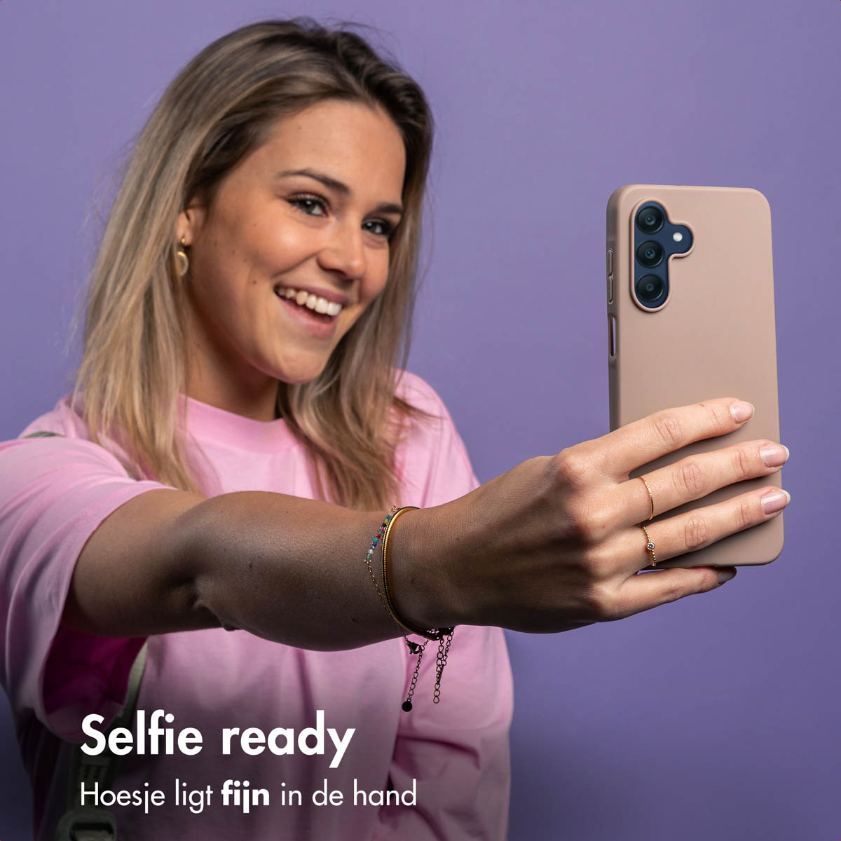 Femme prenant un selfie avec un téléphone dans une coque rose, souriante.