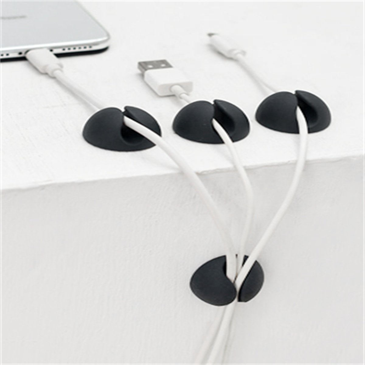 Weiße Kabel, die von schwarzen Haltern auf einer weißen Oberfläche gehalten werden.
