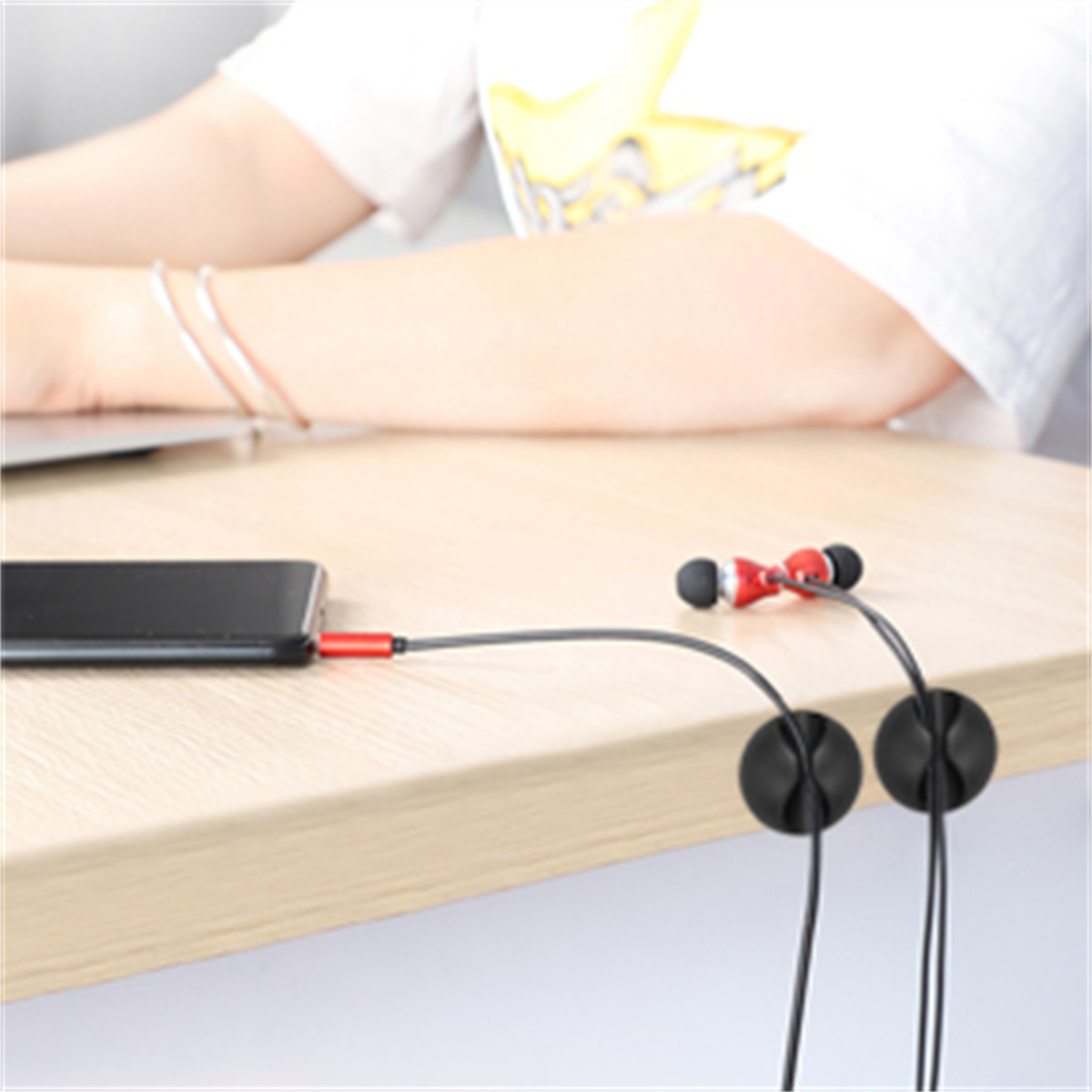 Schwarzes Telefon mit rotem Kabel, das mit schwarzen und roten Kopfhörern verbunden ist. Zwei schwarze Kabelclips sind sichtbar.