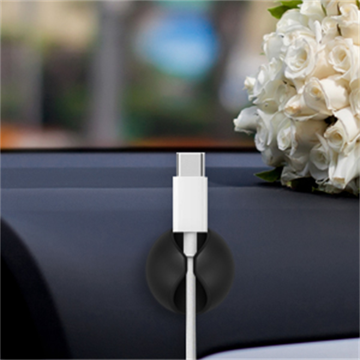 Ein weißes Ladekabel, das von einem schwarzen Kabelorganisator gehalten wird, in der Nähe eines Straußes weißer Blumen in einem Auto.