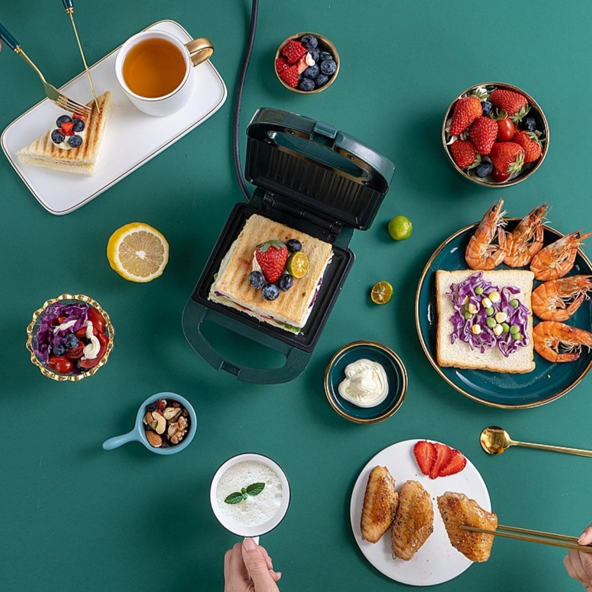 Tisch mit verschiedenen Speisen: Sandwiches, Garnelen, Flügel, Beeren, Nüsse und Tee, Draufsicht.