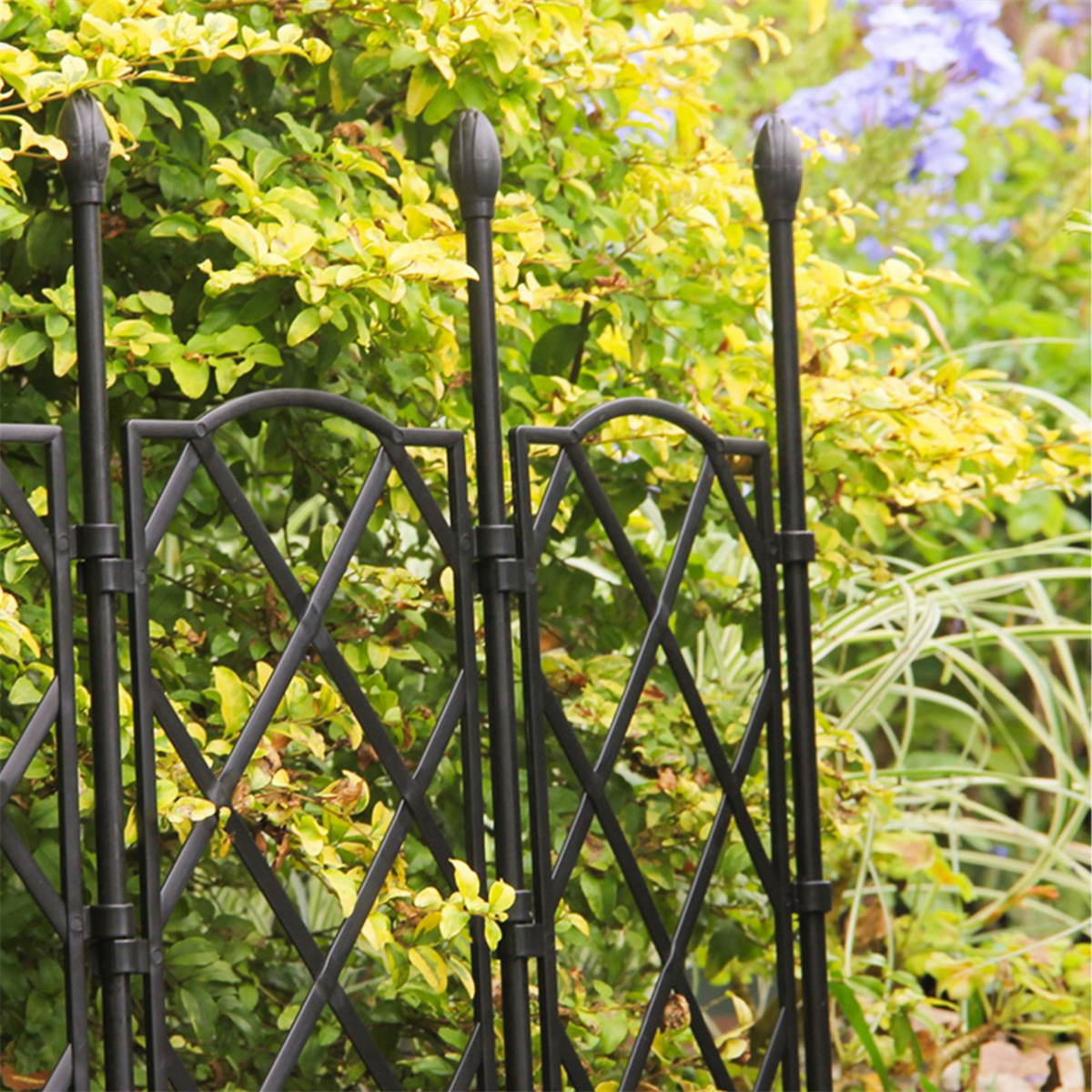 Schwarzer Metallgitterzaun mit grünen Pflanzen und gelben Blumen.