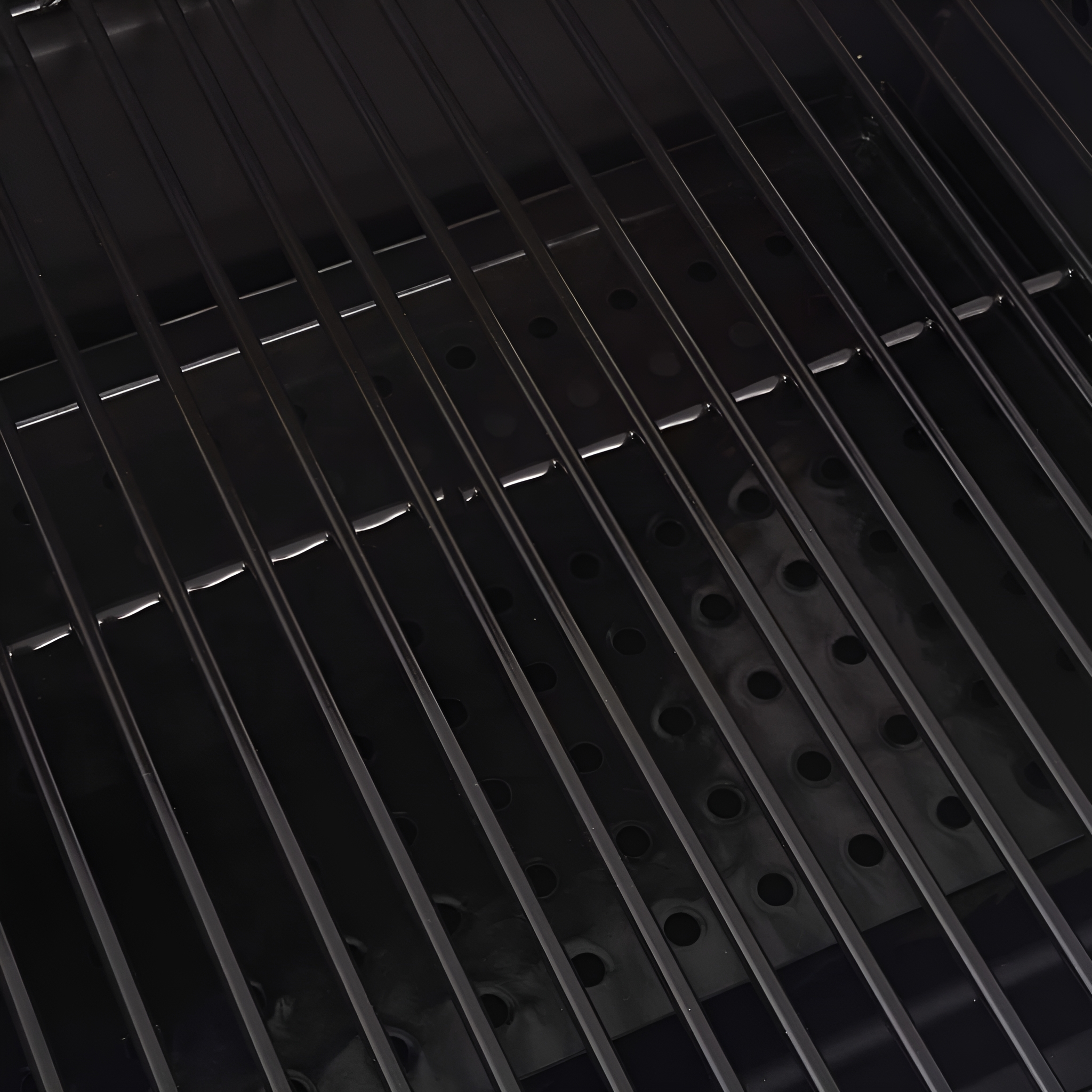 Nahaufnahme eines schwarzen Grills mit parallelen Stäben und perforierter Metalloberfläche darunter.