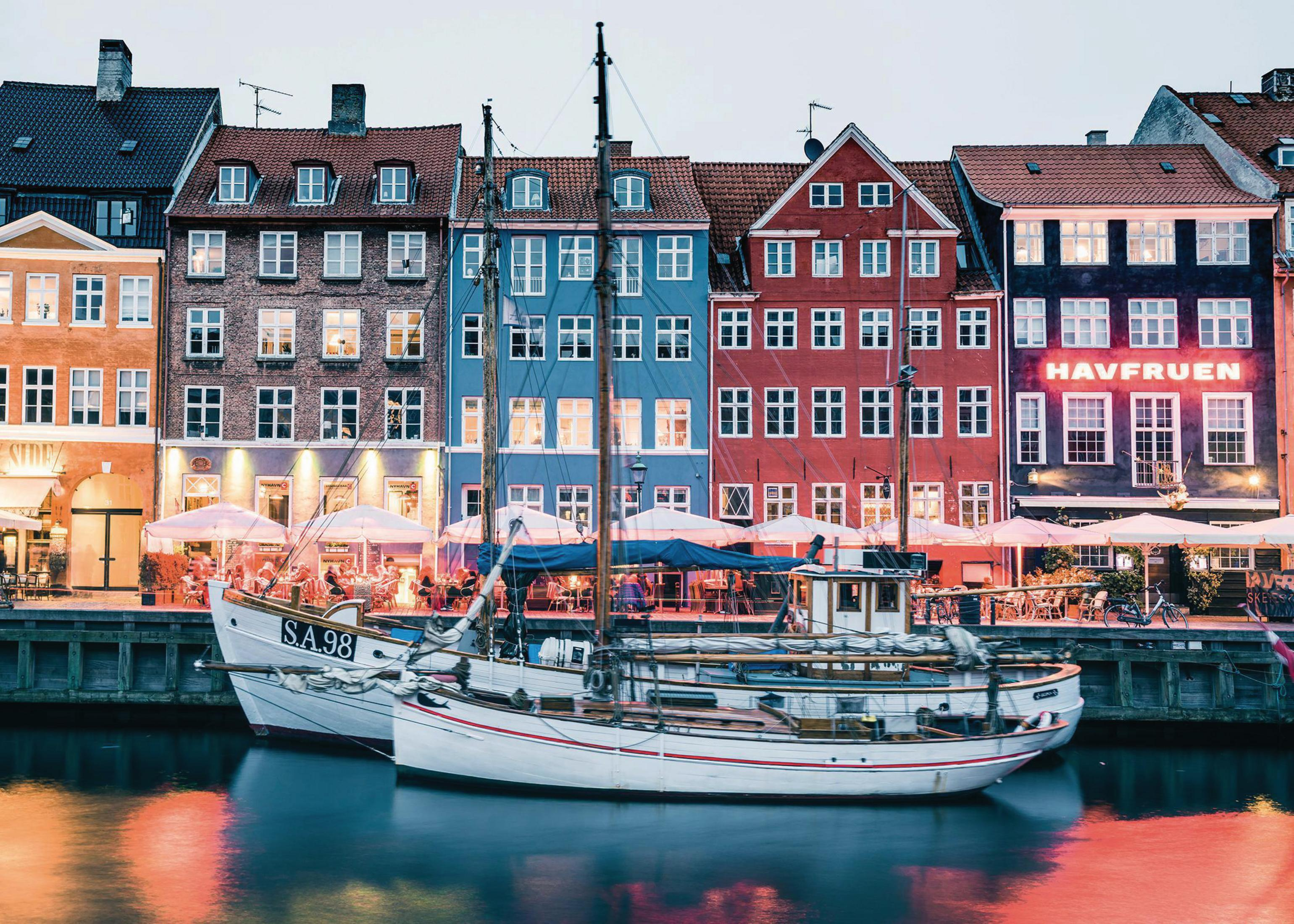 Ein Kanal mit bunten Gebäuden und Booten. Die Gebäude sind verschiedenfarbig, und zwei weiße Boote liegen am Kai.