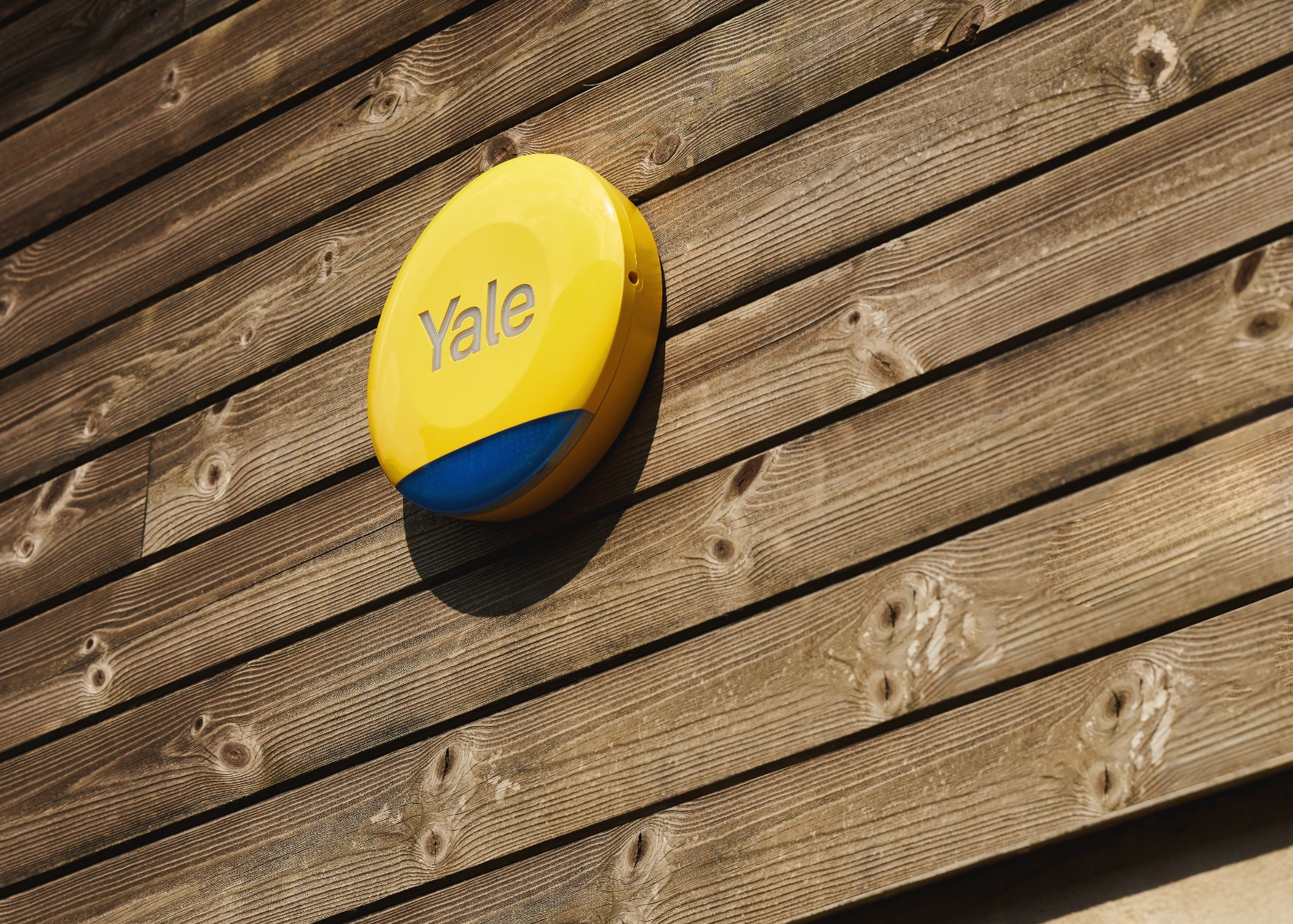 Un allarme di sicurezza Yale giallo attaccato a una parete di legno. L'allarme ha una sezione blu.