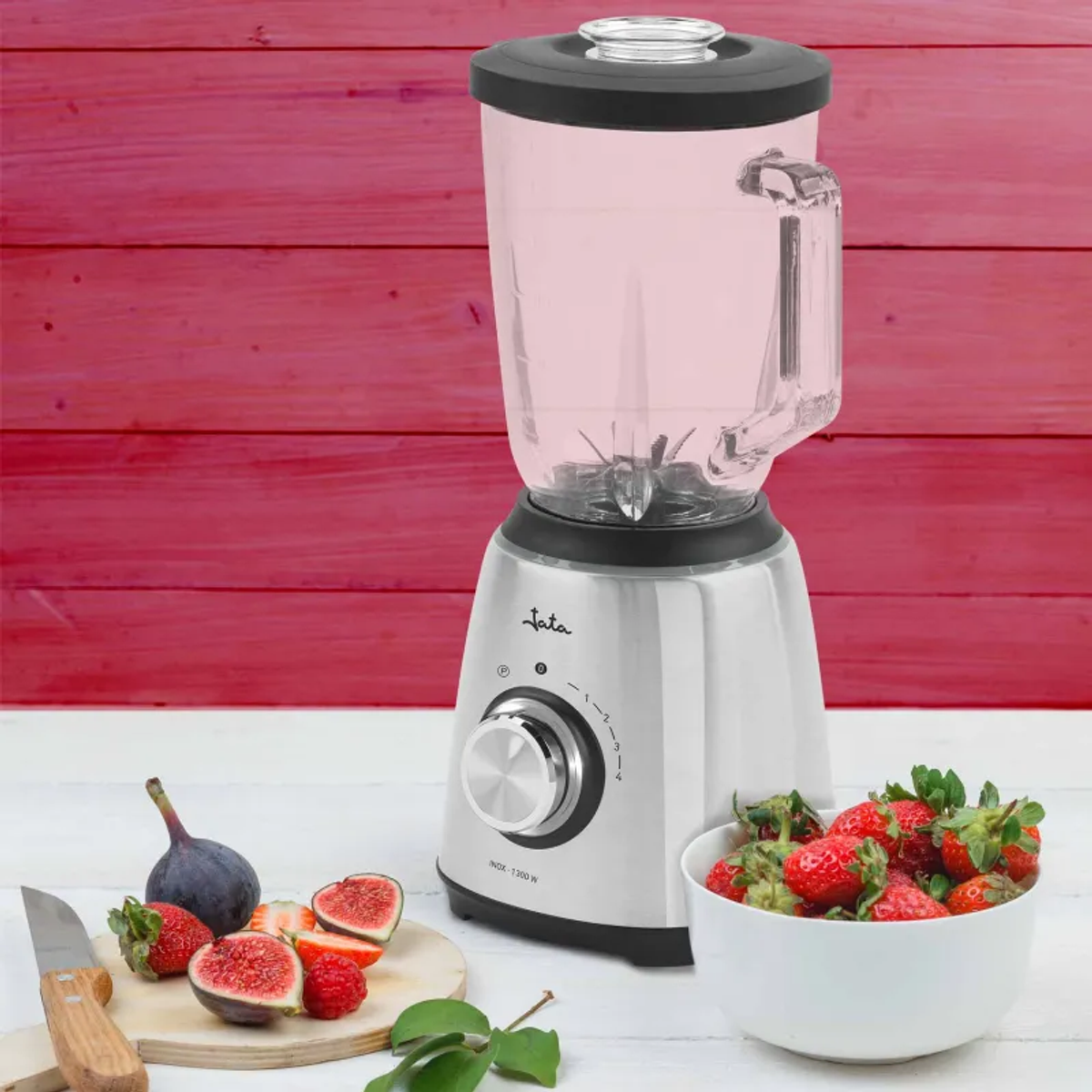 La imagen muestra una licuadora con un recipiente rosa, junto a higos y fresas en una tabla de cortar de madera y un cuenco.