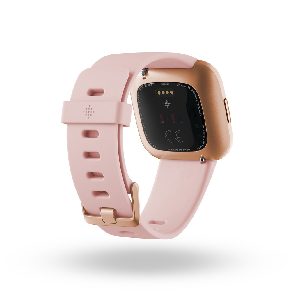 Reloj inteligente rosa y dorado, parte trasera hacia arriba, mostrando sensores y marcas, con banda rosa.