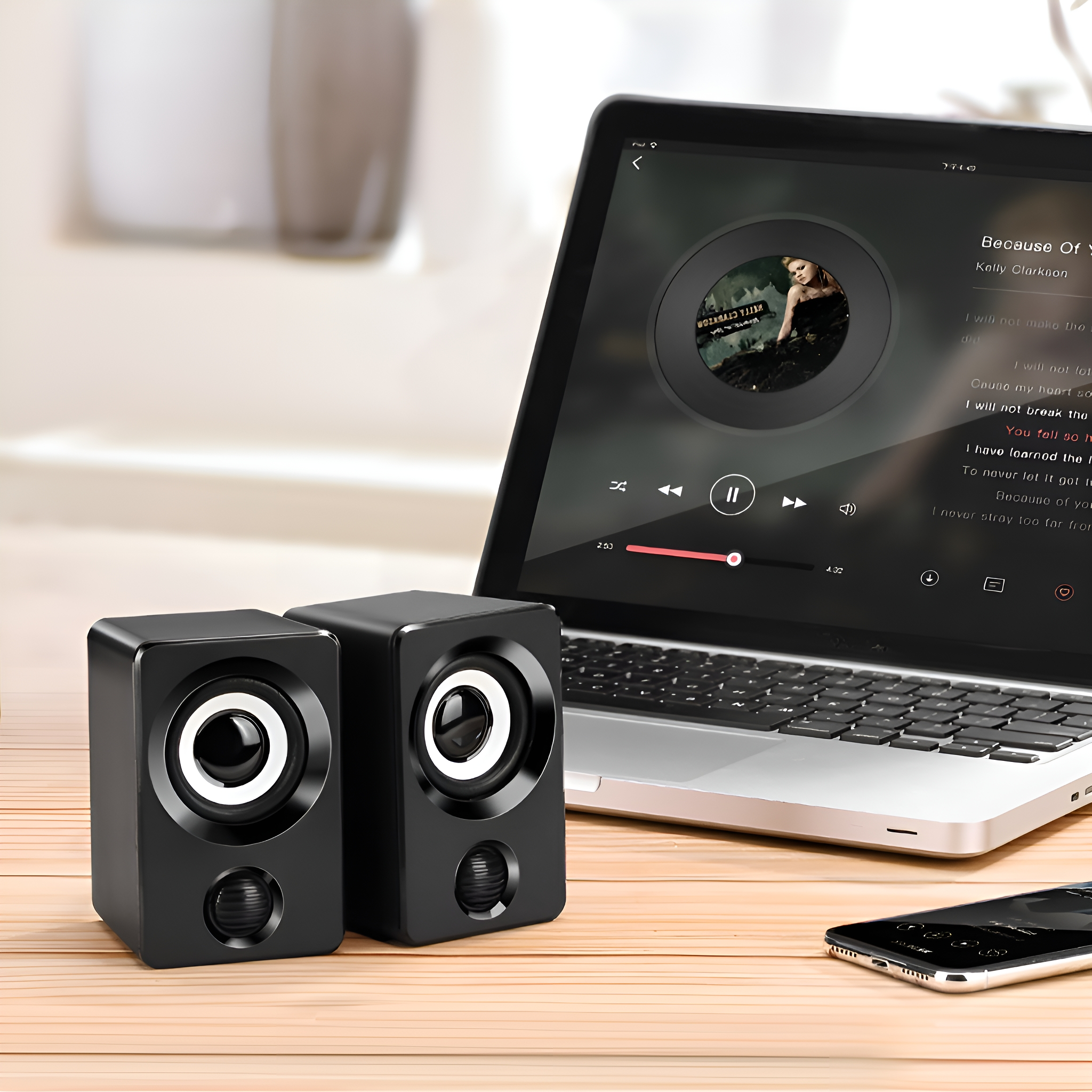 Schwarze Lautsprecher auf Holzoberfläche, mit Laptop, der Musik abspielt, und Smartphone.
