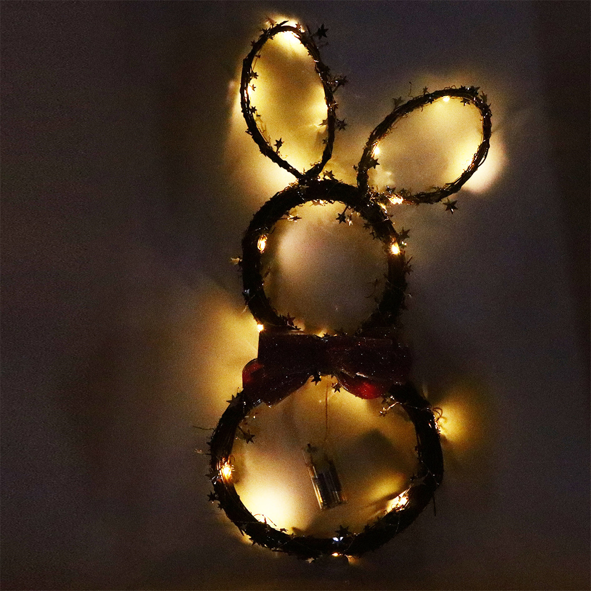 Hasenförmige Lichtdekoration mit roter Schleife und leuchtenden Lichtern auf dunklem Grund.