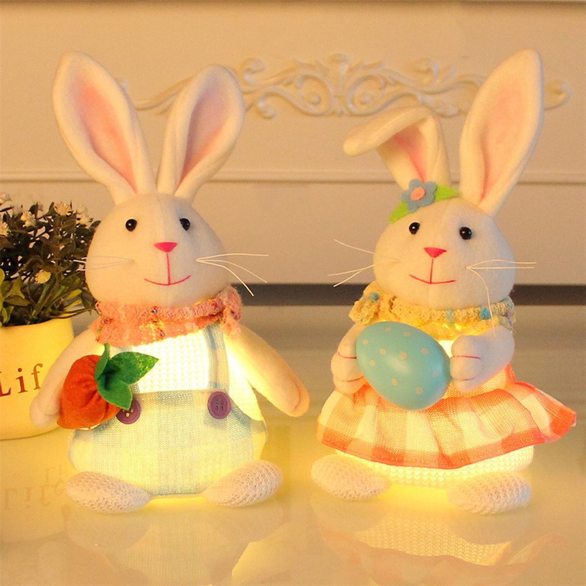 Zwei beleuchtete Osterhasenfiguren. Einer hält eine Karotte, der andere ein Osterei.
