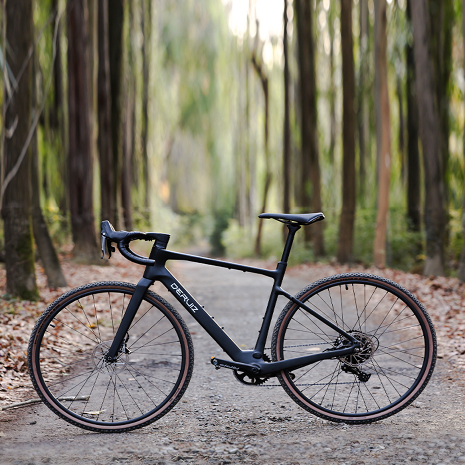 Schwarzes Rennrad auf einem Schotterweg mit Bäumen im Hintergrund. Das Fahrrad hat einen schwarzen Rahmen und braune Reifen.