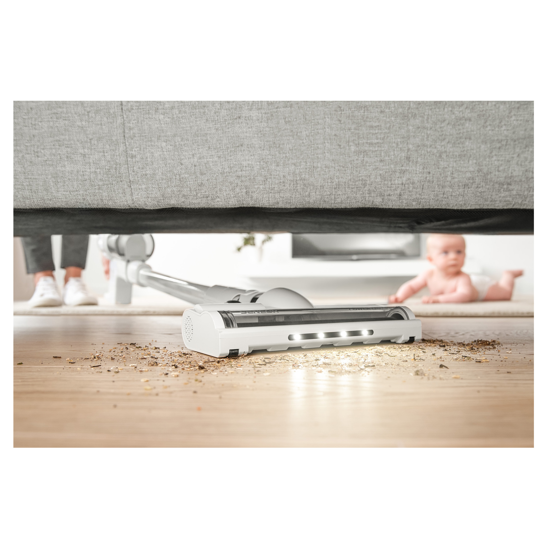 Testa dell'aspirapolvere che pulisce il pavimento. Bambino e gambe visibili sullo sfondo.
