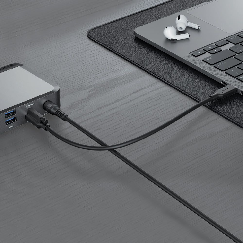 Laptop collegato a un power bank e auricolari su una scrivania in legno. Tappetino nero.