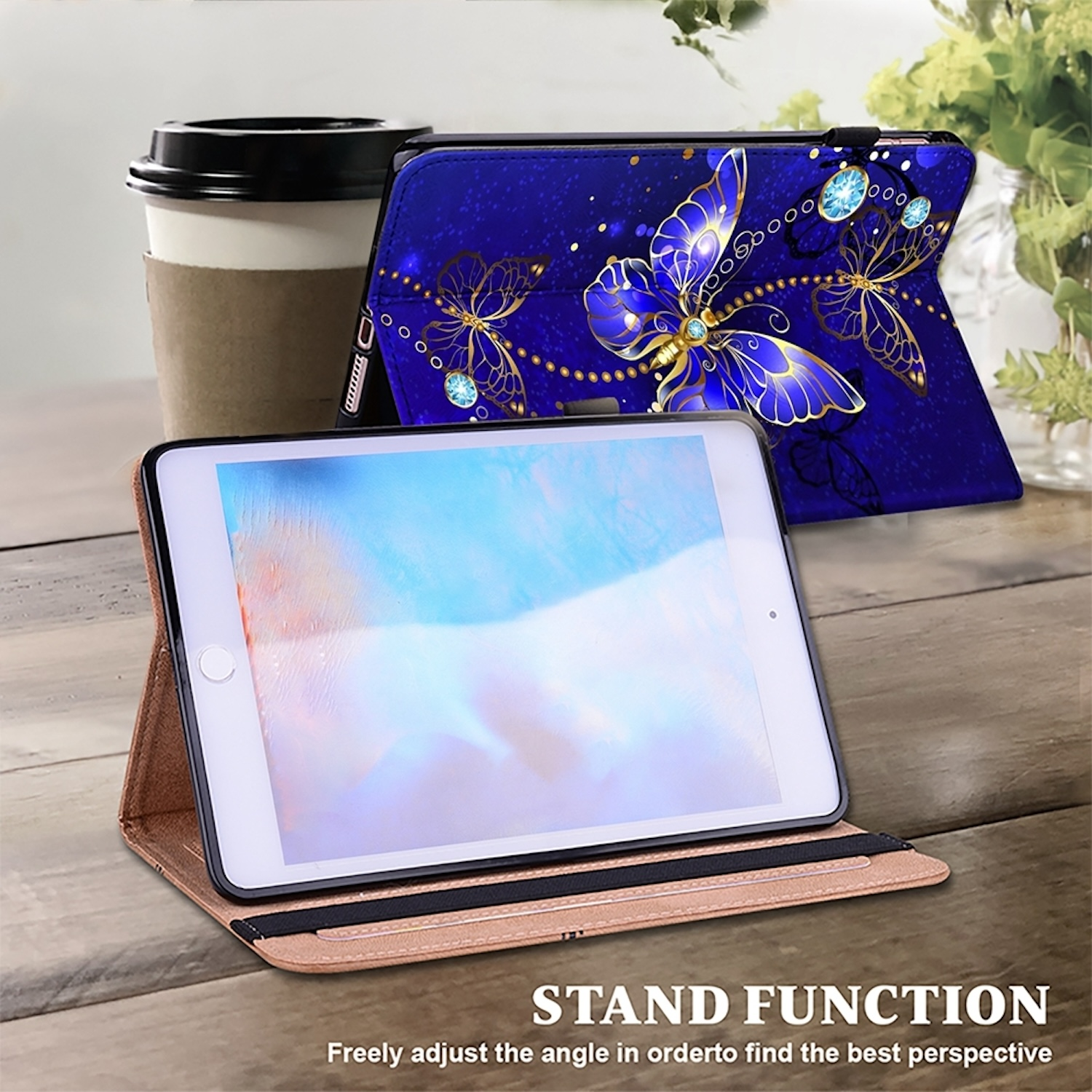 Ein Tablet in einer blauen Hülle mit Schmetterlingsdesign, auf einem Tisch neben einer Kaffeetasse und einer Pflanze.