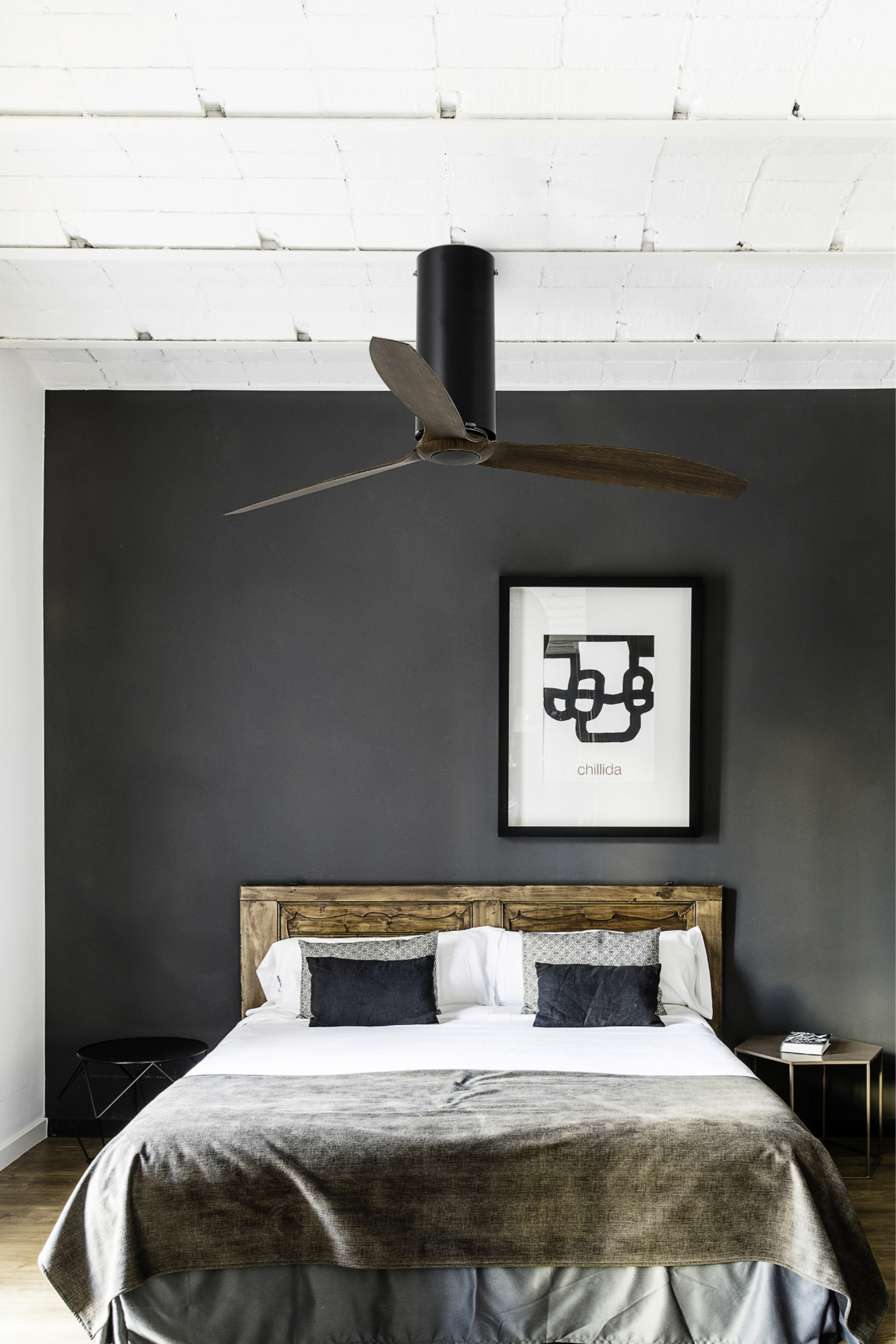 Schlafzimmer mit Bett, dunkelgrauer Wand, Kunst und Deckenventilator.