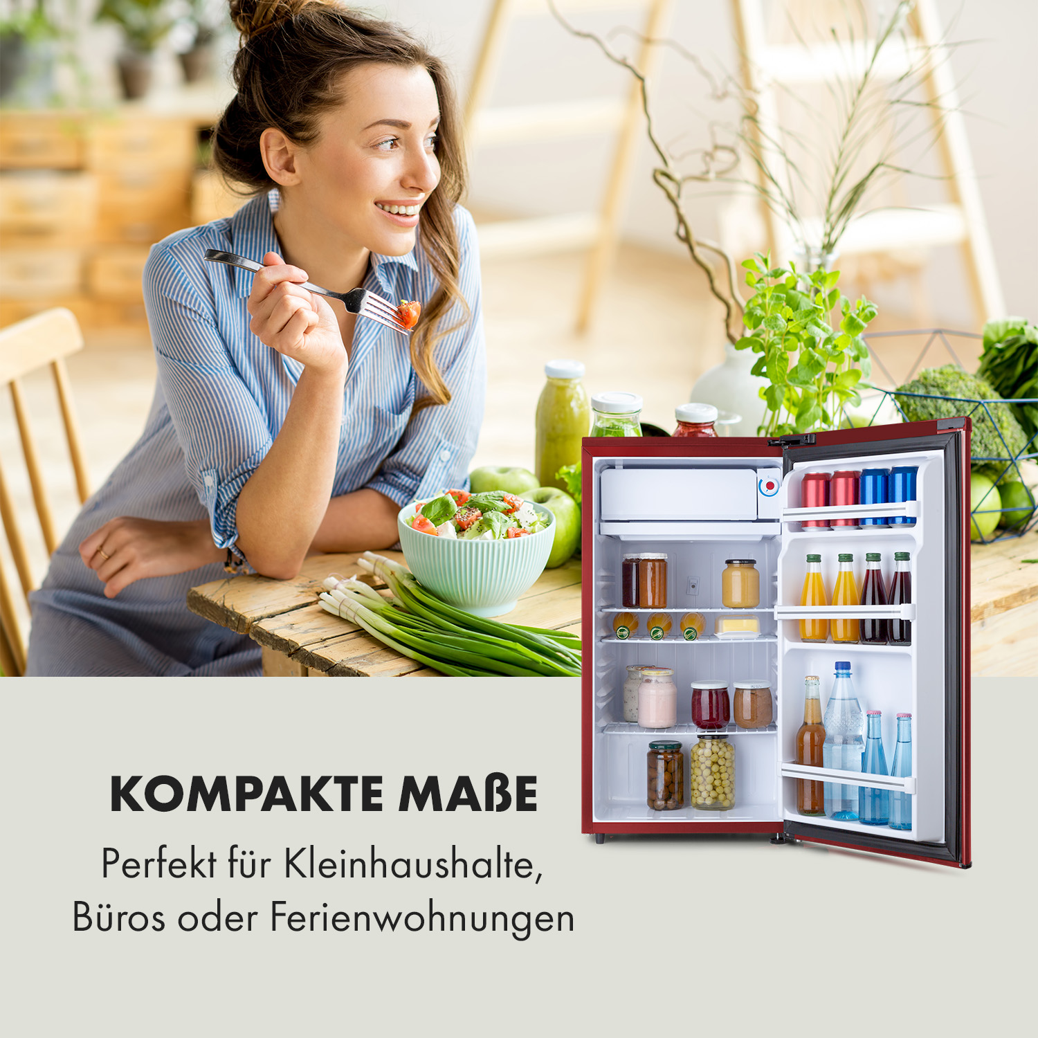 Eine Frau lächelt neben einem roten Mini-Kühlschrank. Die Kühlschranktür ist geöffnet und zeigt Lebensmittel und Getränke.