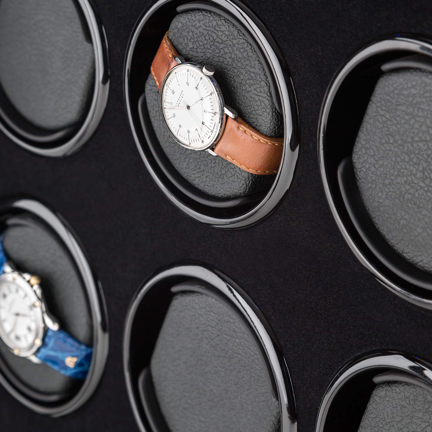 Ein schwarzer Uhrenbeweger mit mehreren Uhren darin. Eine Uhr mit braunem Armband ist sichtbar.