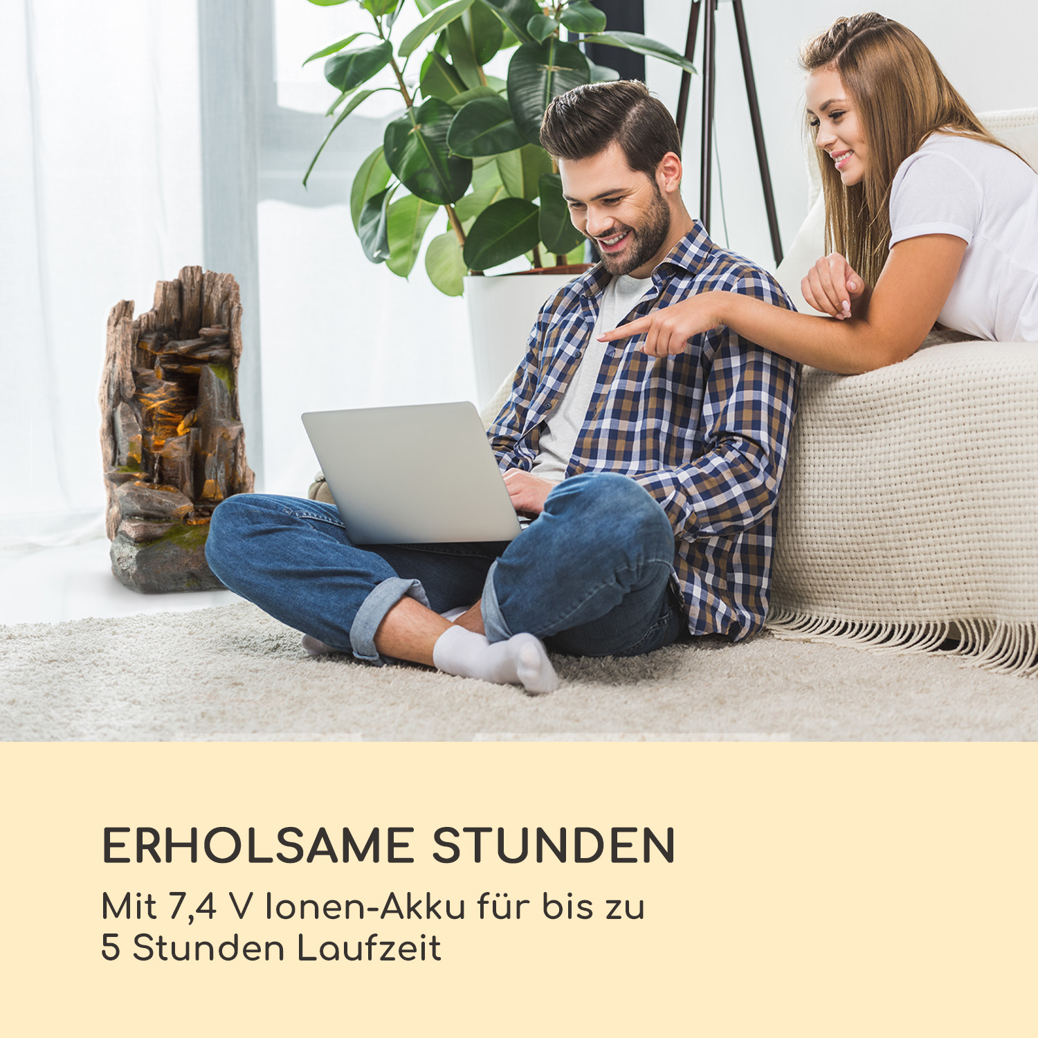 Ein Paar sitzt im Wohnzimmer auf einem Sofa und schaut auf einen Laptop. Links ist ein dekorativer Brunnen.