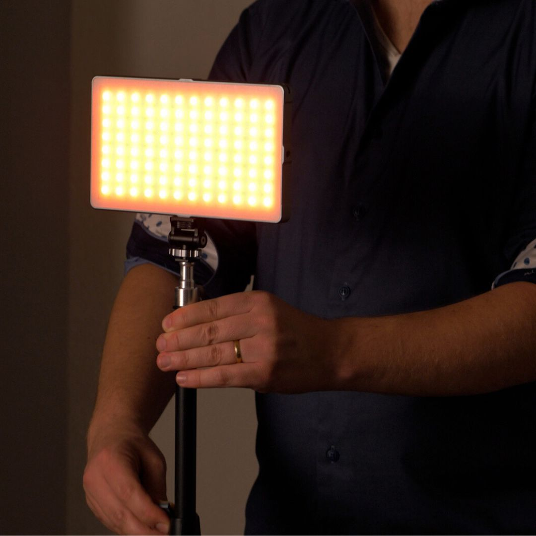 A man holding a rectangular LED light. The light is on, emitting a warm, yellow glow.