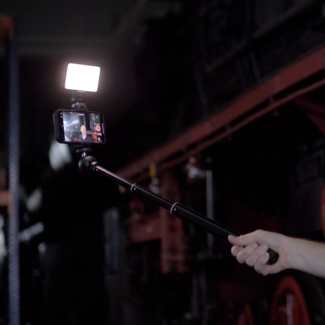 Person holding a smartphone with a light attached, filming in front of a red background.