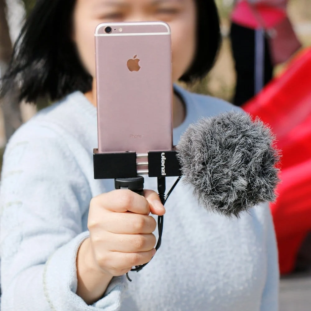 Une personne tient un téléphone avec un microphone attaché. Le téléphone est dans un support.