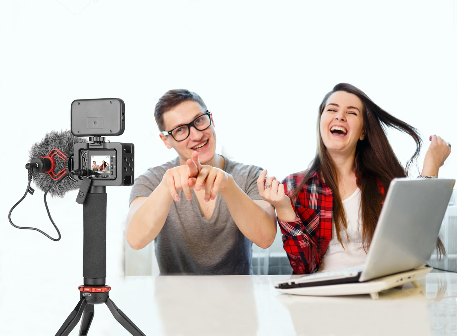 Deux personnes riant font une vidéo. L'un pointe vers la caméra sur un trépied. Ordinateur portable en arrière-plan.