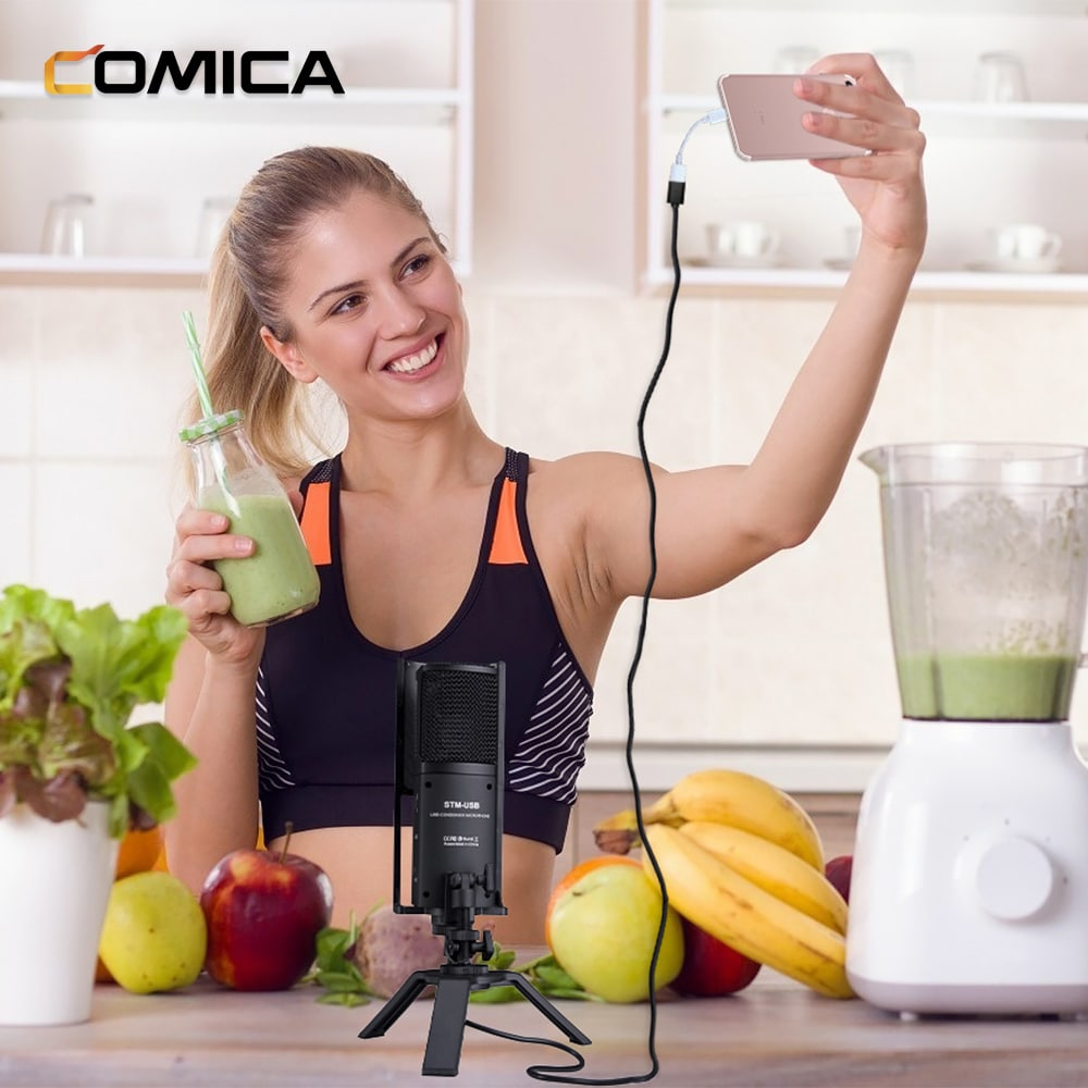 Een vrouw neemt een video op, houdt een telefoon vast, met een microfoon op tafel. Er is fruit en groenten.