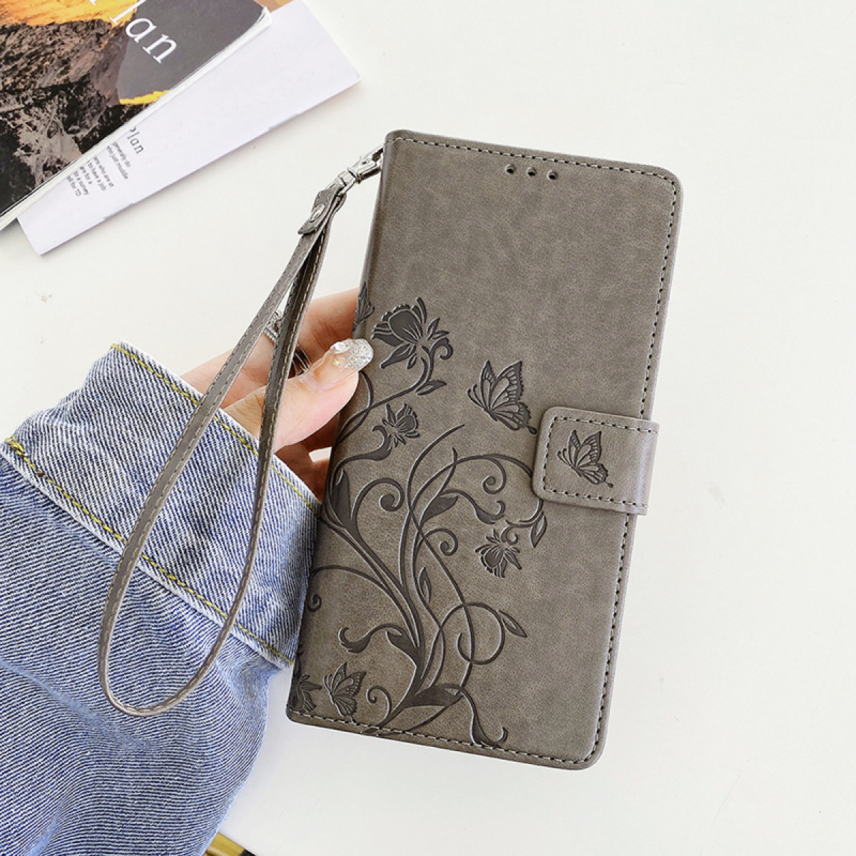 Una custodia grigia per telefono con un design floreale e dettagli a farfalla.