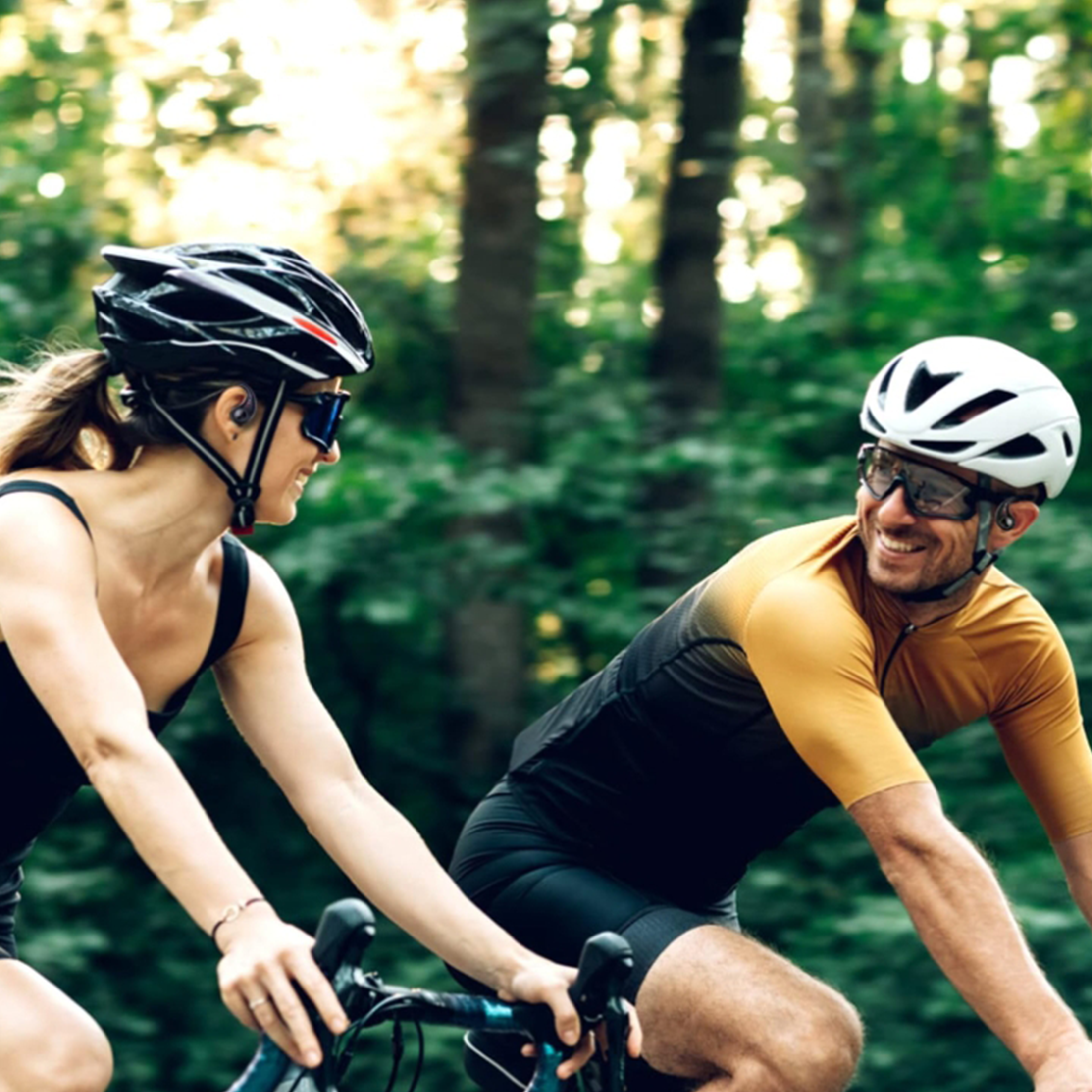 Zwei Radfahrer fahren auf einem Weg durch einen Wald. Sie tragen Helme und Sonnenbrillen.