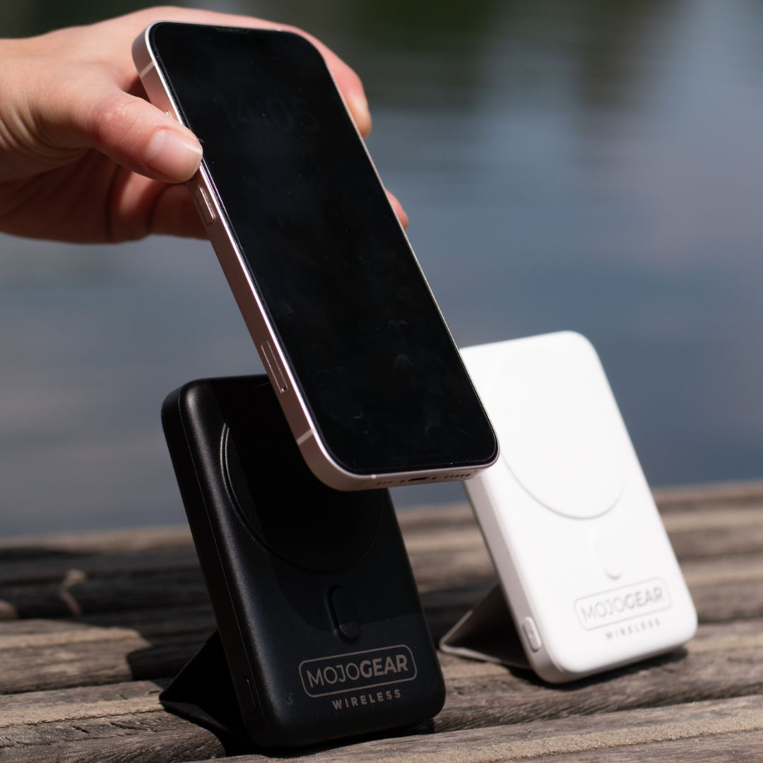 Een hand die een telefoon boven twee draadloze opladers houdt, één zwart en één wit.