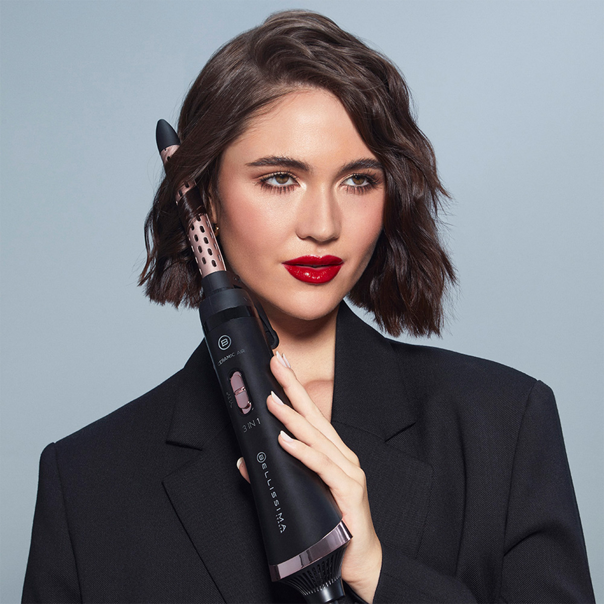 Frau mit rotem Lippenstift hält Lockenstab, schwarze Jacke.