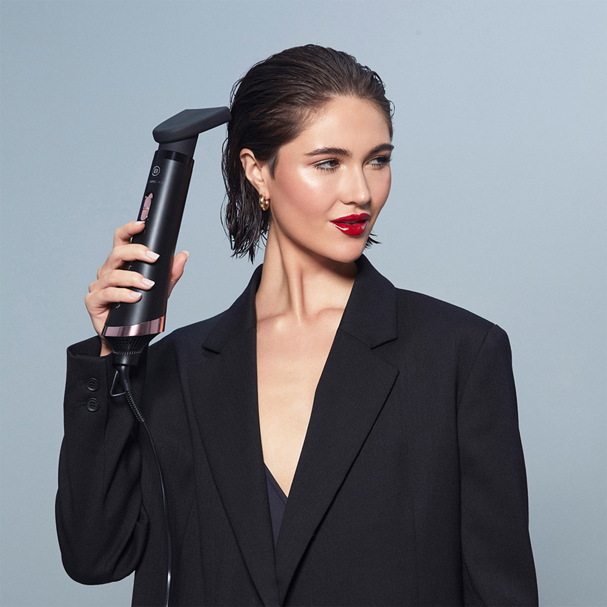 Eine Frau in einem schwarzen Blazer verwendet ein schwarz-roségoldenes Haarstyling-Tool.