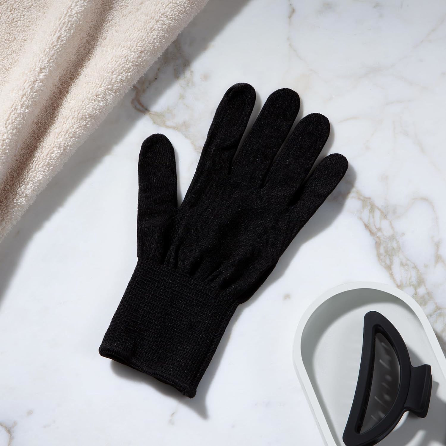 Schwarze Handschuhe auf Marmor. Ein Handtuch und eine Haarspange liegen daneben.