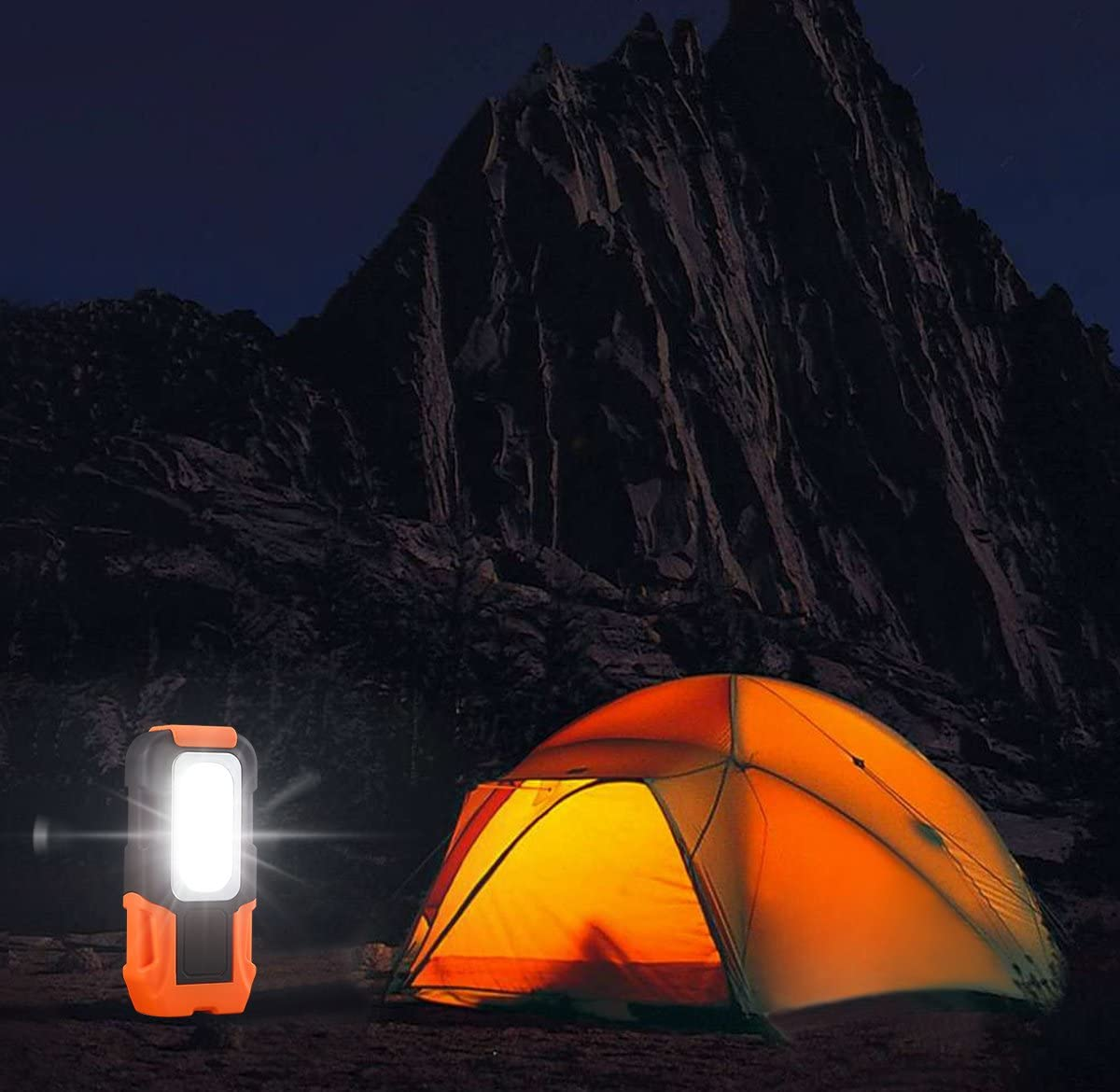 Ein leuchtendes orangefarbenes Zelt und eine Taschenlampe in dunkler, felsiger Landschaft bei Nacht.