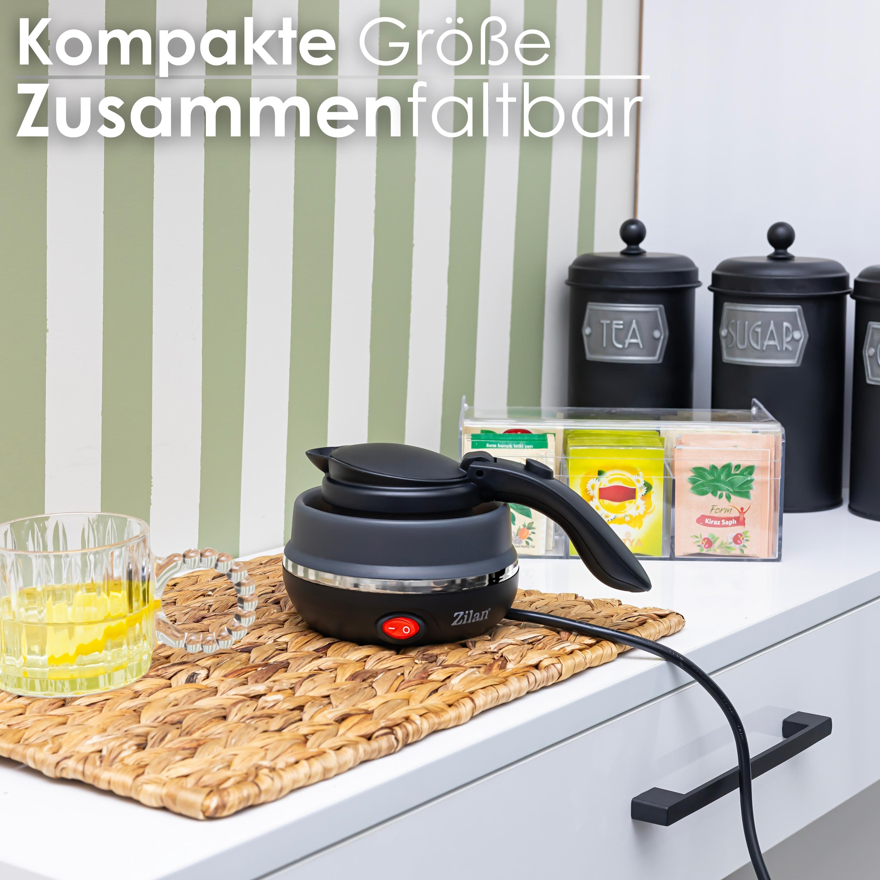 Schwarzer Wasserkocher auf einer Matte mit einem Glas Flüssigkeit und Teebehältern.
