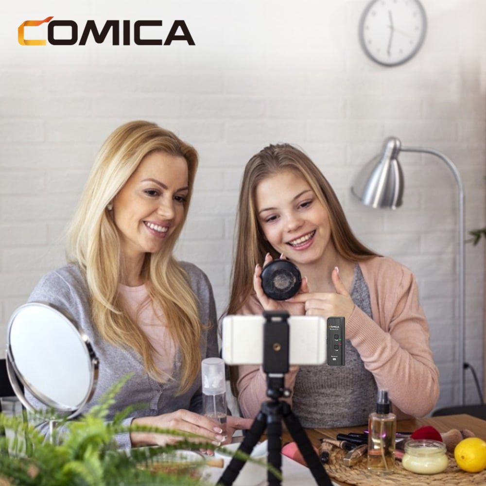 Twee vrouwen filmen. Eén houdt een kleine microfoon vast. Er staat apparatuur op tafel.