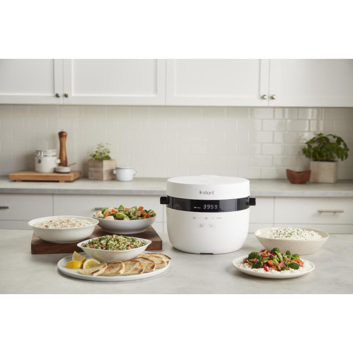 An Instant brand white rice cooker. Bowls of food and ingredients are arranged around it.