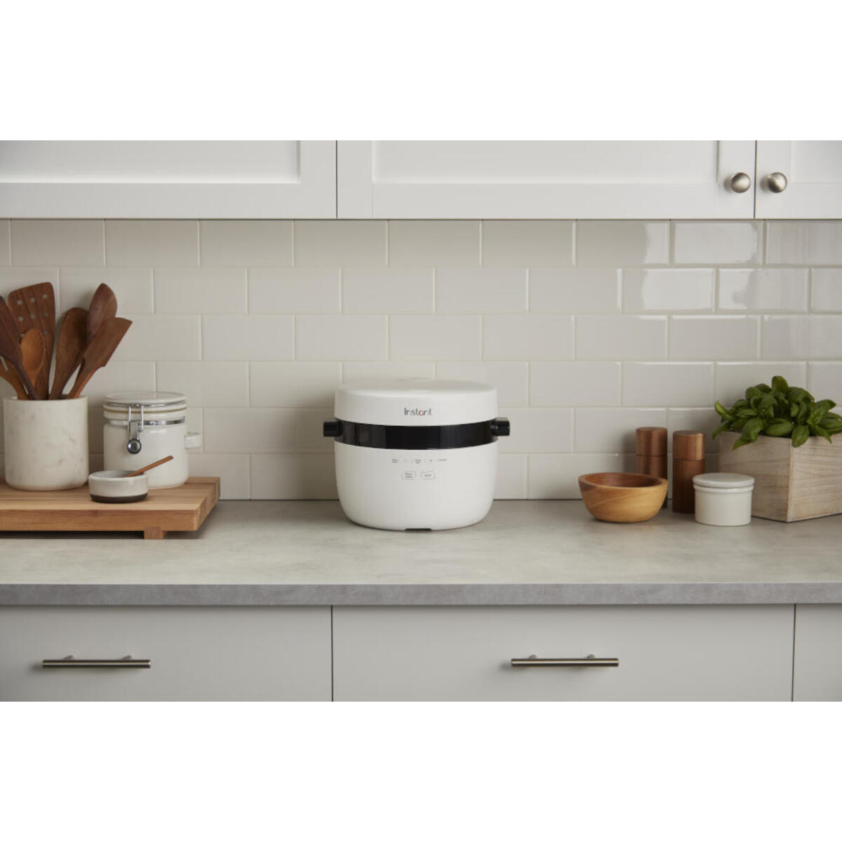 White Instant pot on counter. Wooden spoons and basil on left. Kitchen in the background.