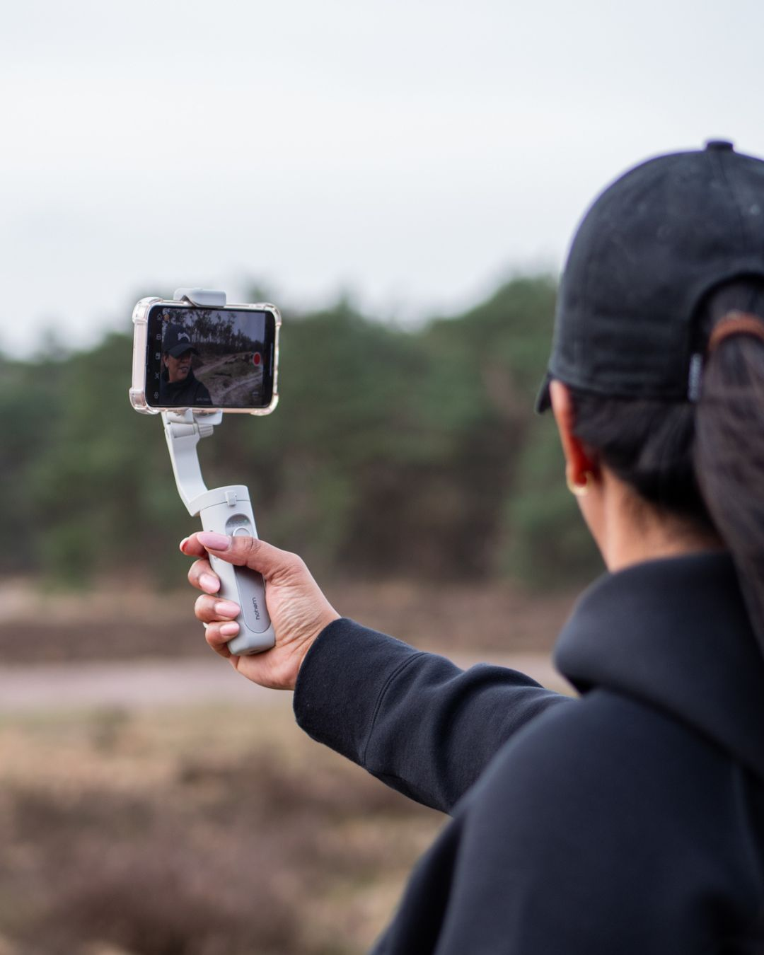 Personne filmant avec un téléphone sur un stabilisateur. Arrière-plan : arbres et ciel.