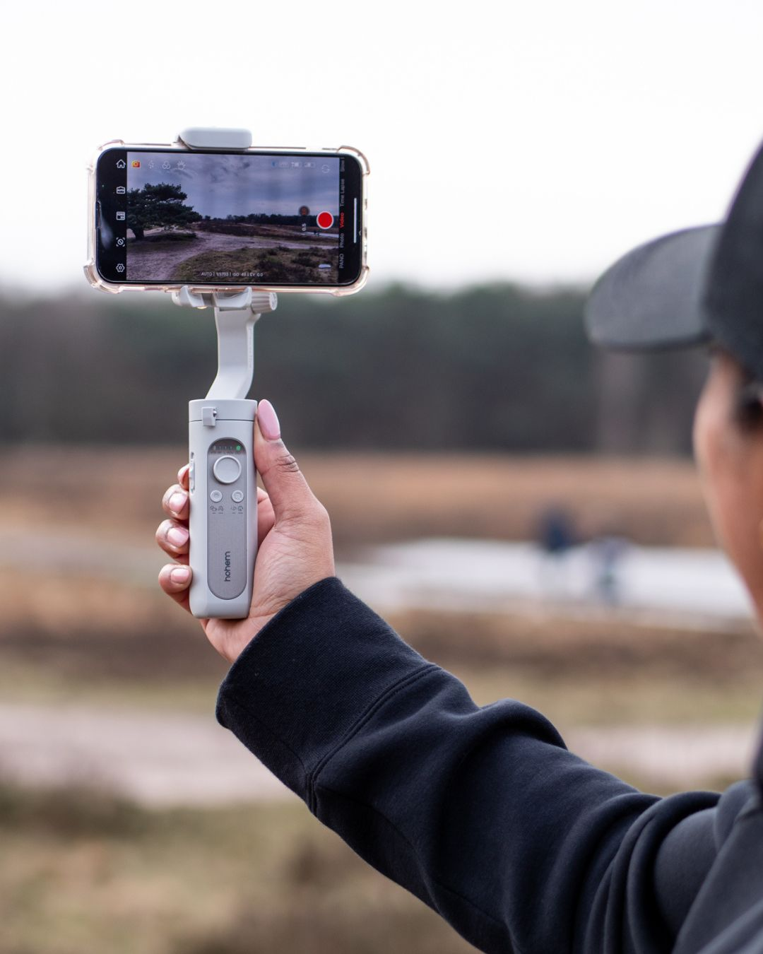 Personne tenant un téléphone sur un gimbal, filmant un paysage.
