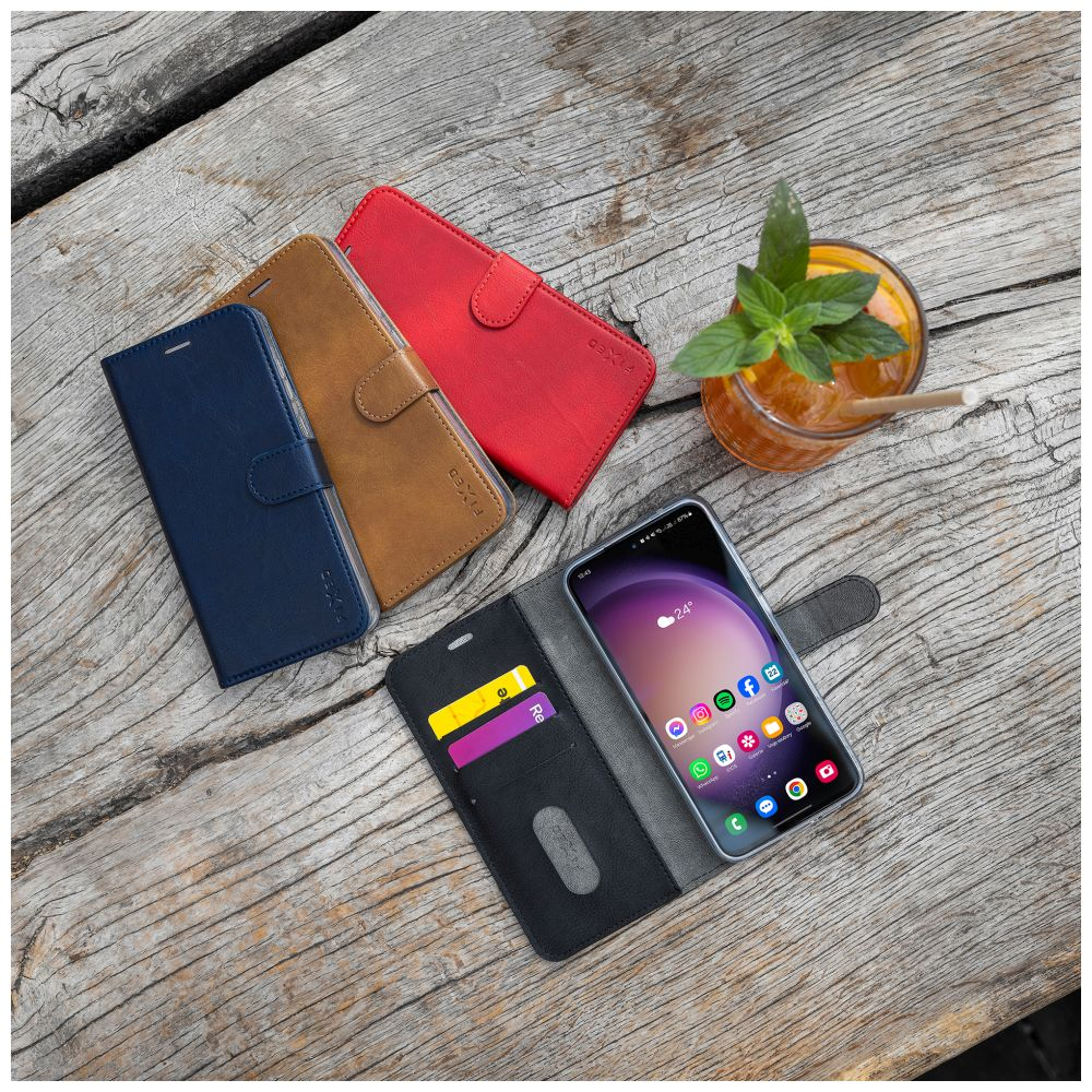 Smartphone in einer Hülle mit anderen Hüllen und einem Getränk auf einem Holztisch. Das Getränk hat einen Strohhalm.