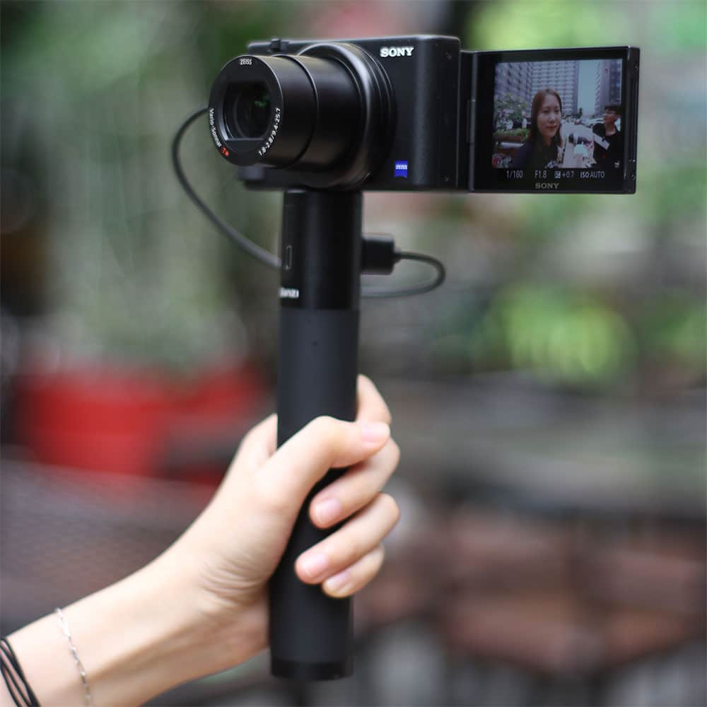 Een persoon houdt een zwarte Sony camera vast met een scherm waarop een vrouw te zien is.