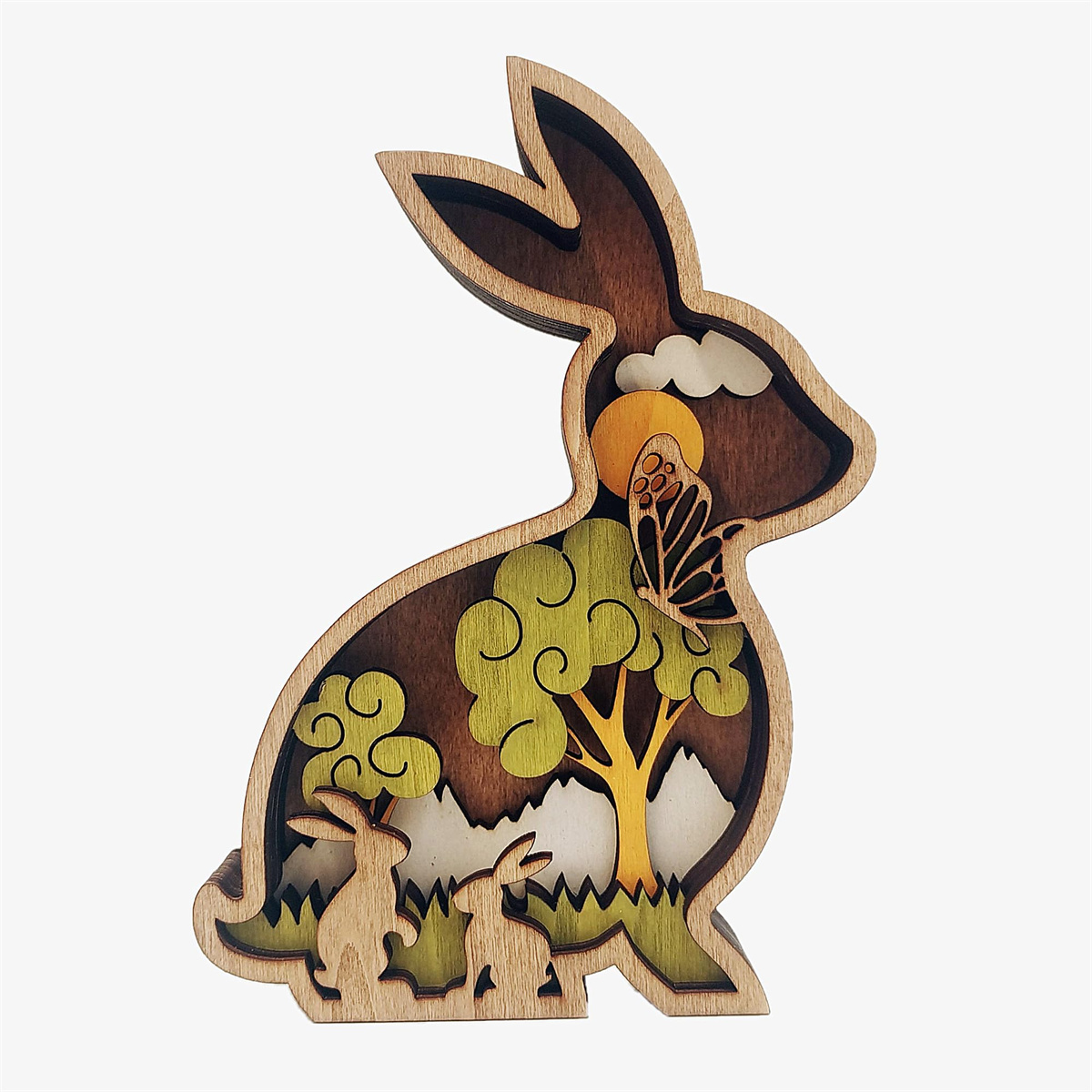 Osterhasen-Dekoration aus Holz mit geschichteten Ausschnitten eines Baumes, Schmetterlings und Landschaft.