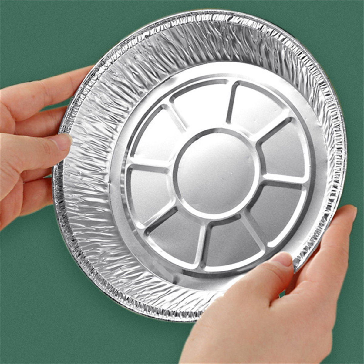 Zwei Hände halten einen runden Aluminiumfolienbehälter mit erhabener Mitte. Grüner Hintergrund.