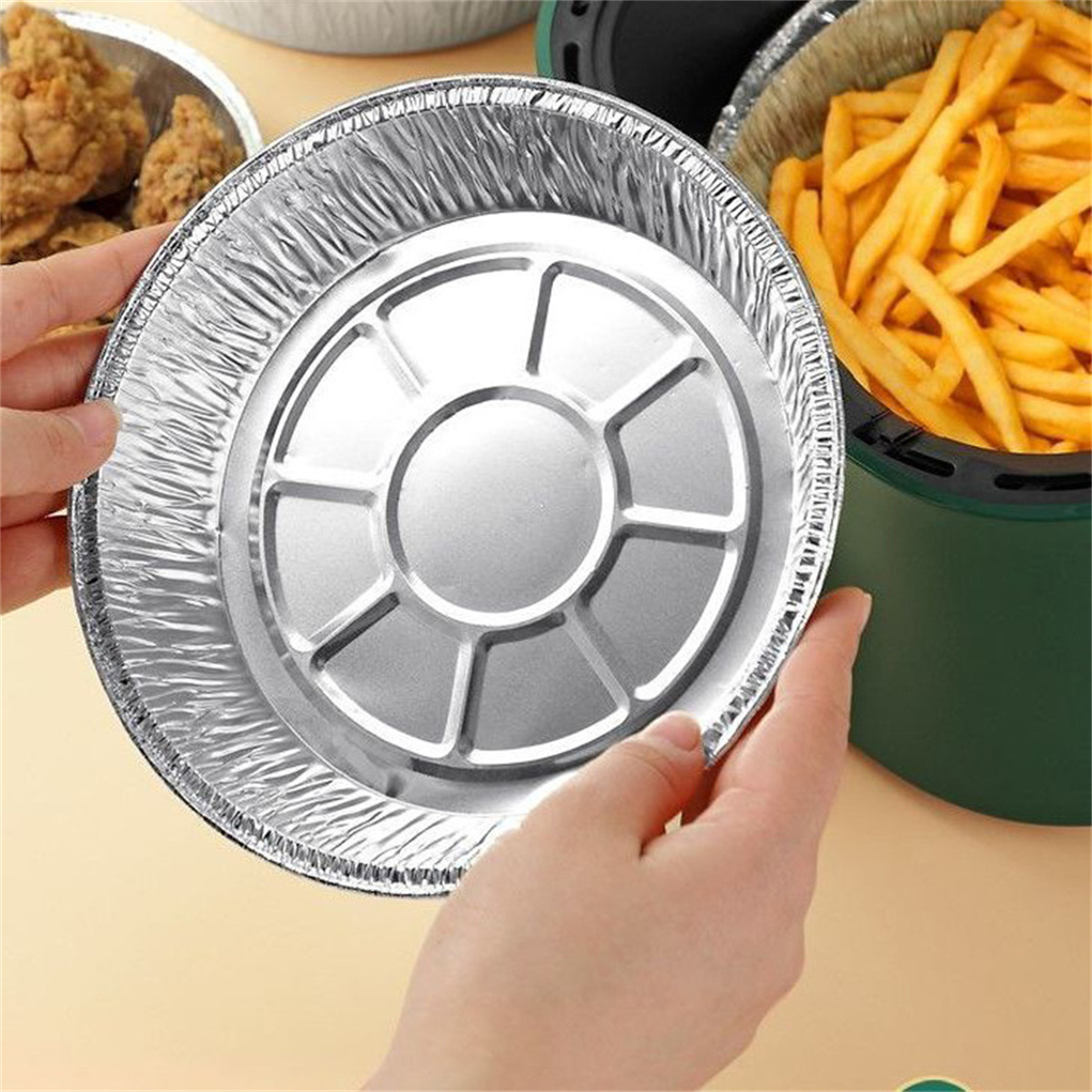 Behälter aus Aluminiumfolie. Eine Hand hält den Behälter, im Hintergrund Pommes Frites.